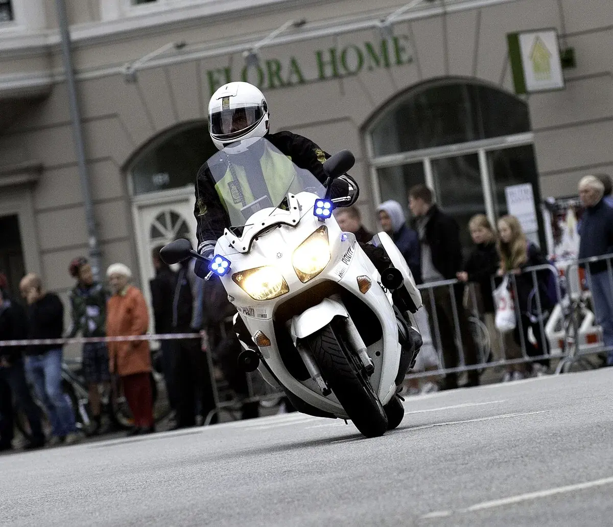 A Danish police motorcycle leaning through a turn during a cycling race with spectators watching behind barriers.