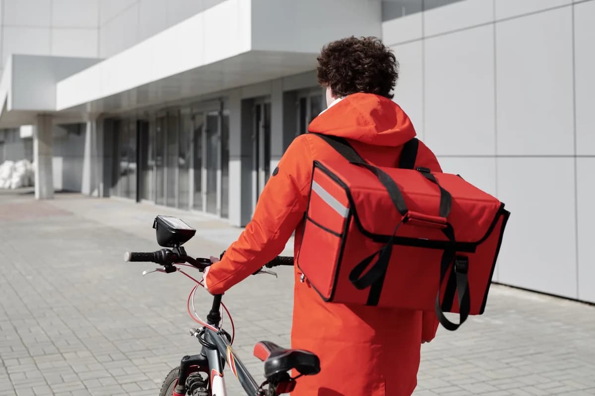 Food delivery courier in a red jacket walking beside a bicycle with an insulated bag