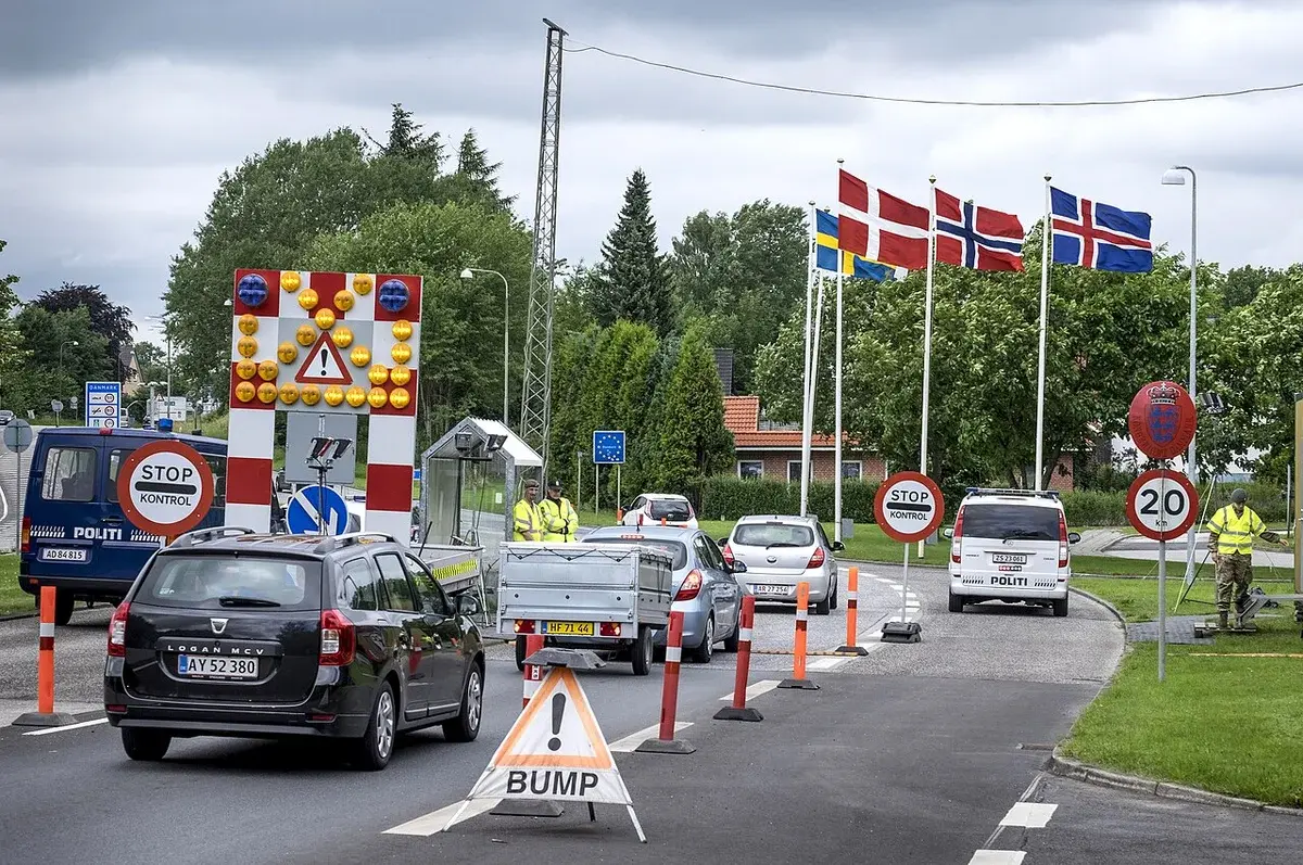 Cars wait at a border control checkpoint with police and inspection signs.