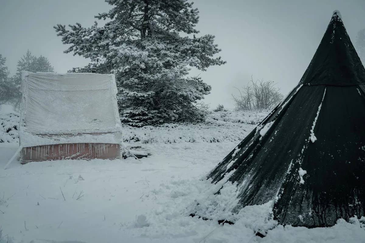 Two tents covered in snow in a winter campsite.