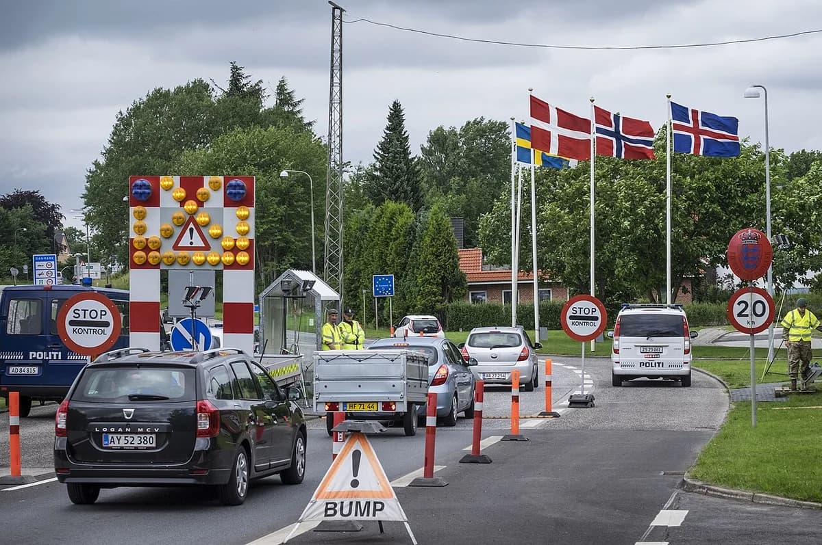 Cars waiting at a Danish border control checkpoint with police and flags.
