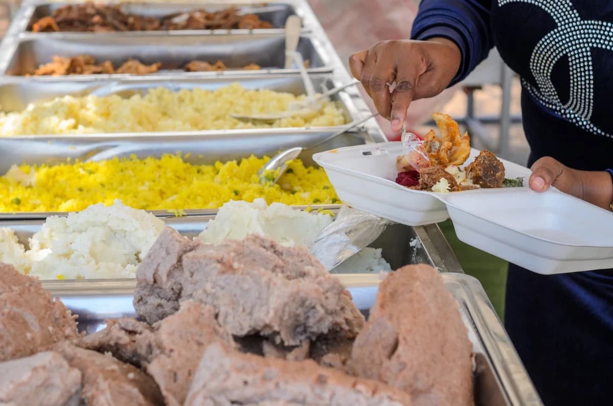 A person serving food from a buffet station into a takeout container.