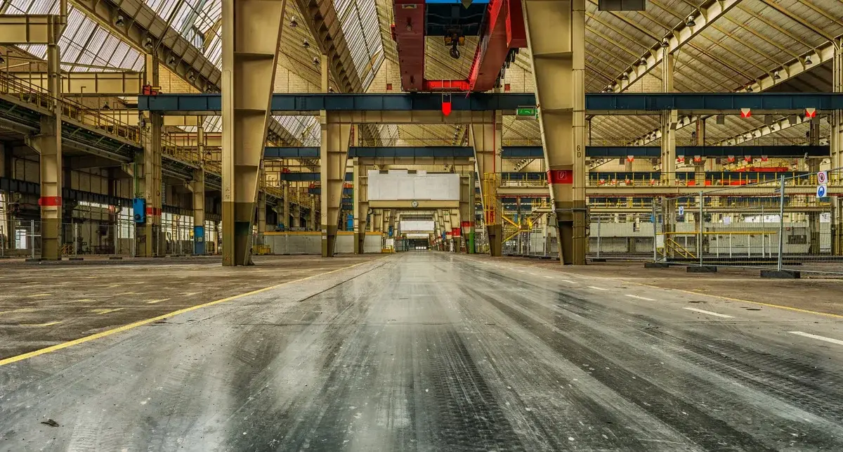 Wide view of an empty warehouse with overhead cranes and metal beams.