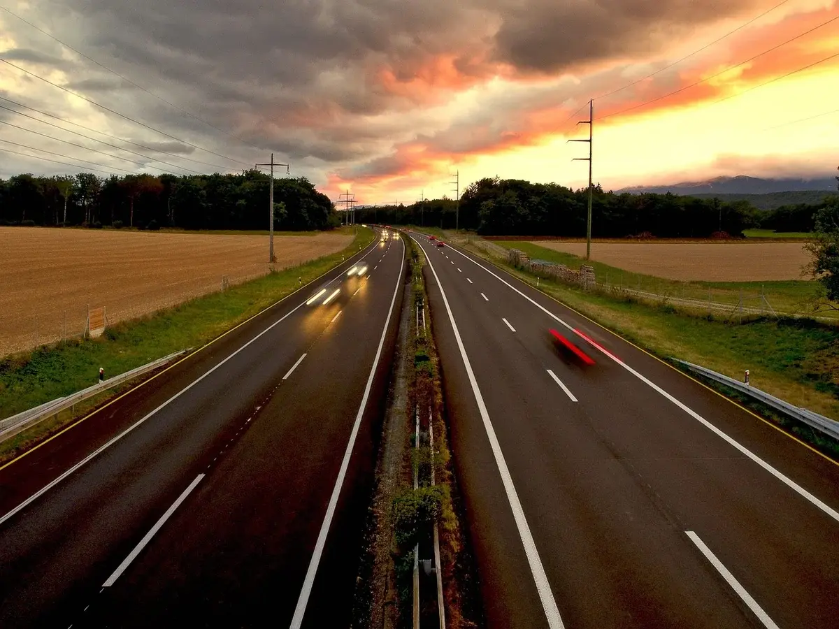 A highway at sunset with cars driving through farmland.