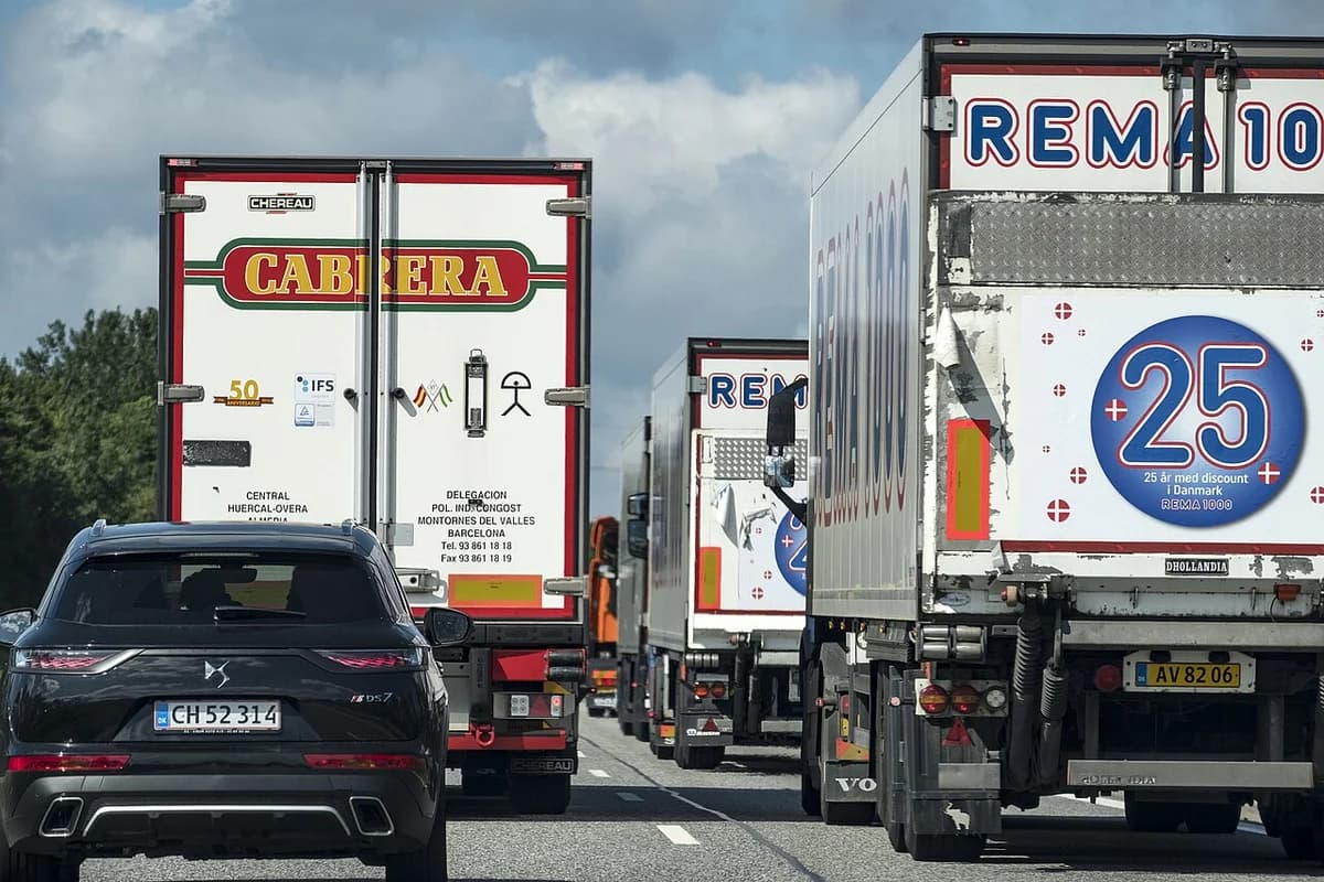 A line of trucks and one black car on a highway under partly cloudy skies.