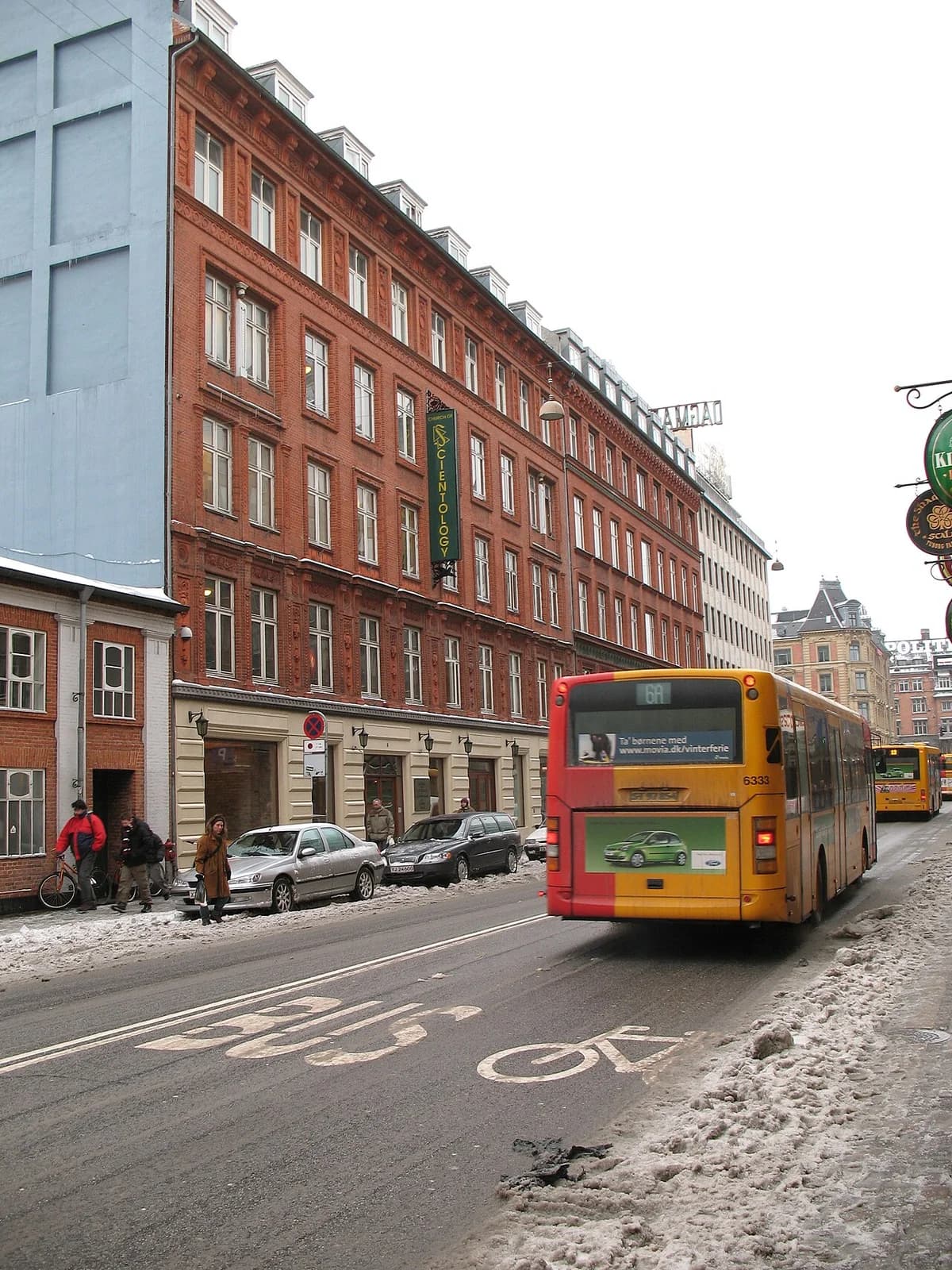 Street with orange buses, red brick buildings, and Church of Scientology sign