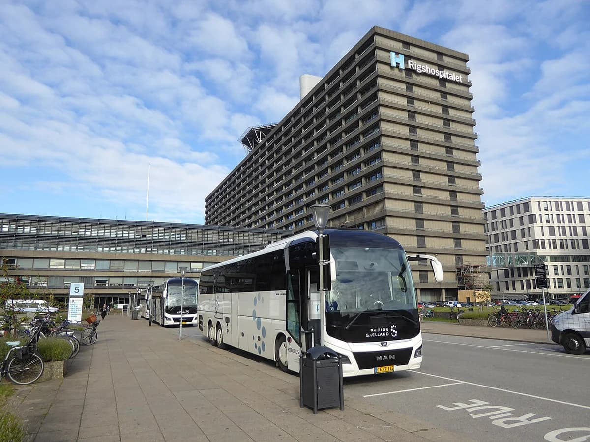 Three white DitoBus coaches parked outside Rigshospitalet hospital in Copenhagen.