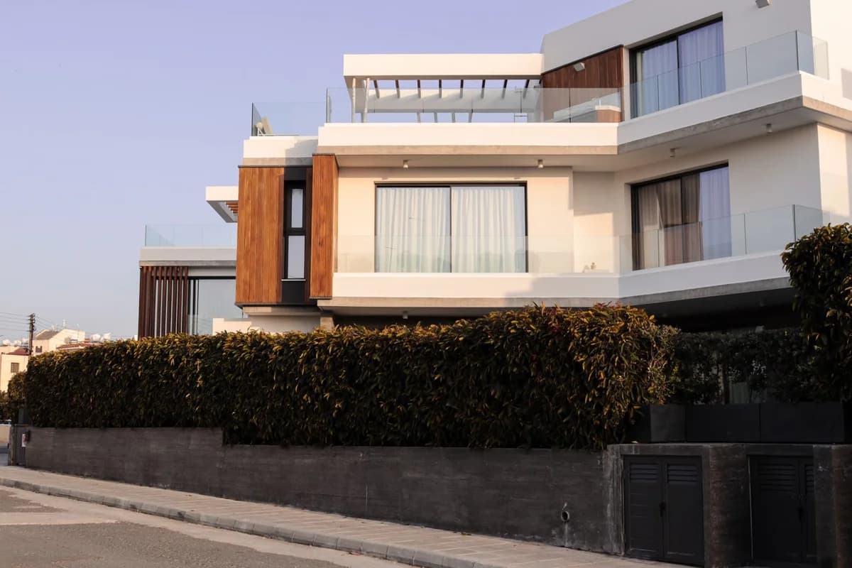 Modern luxury villa with white and wood facade behind green hedges