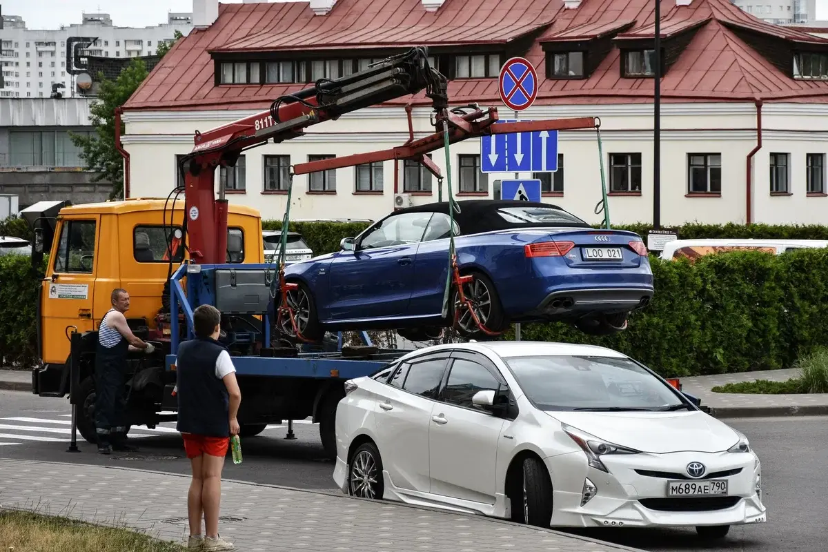 A blue Audi cabriolet is loaded onto a tow truck on a city street.