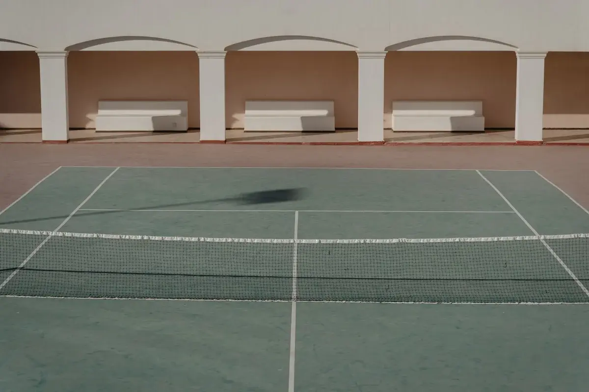 An empty tennis court with benches under arches in daylight.
