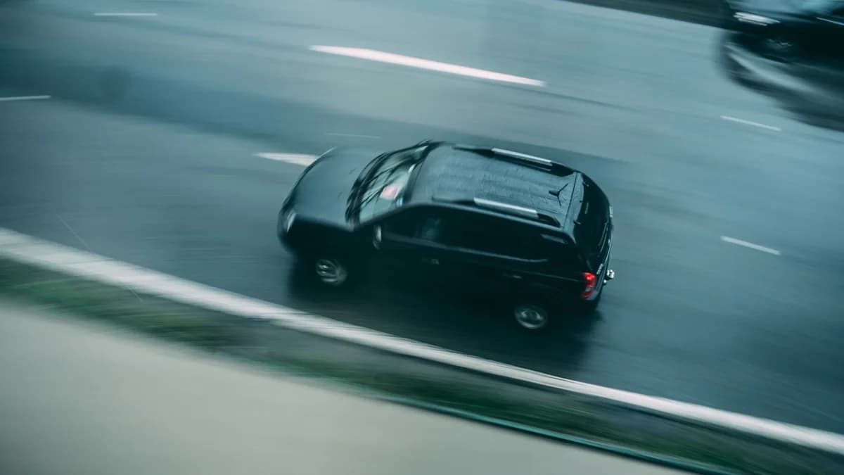 A black SUV speeding on a wet highway with motion blur.