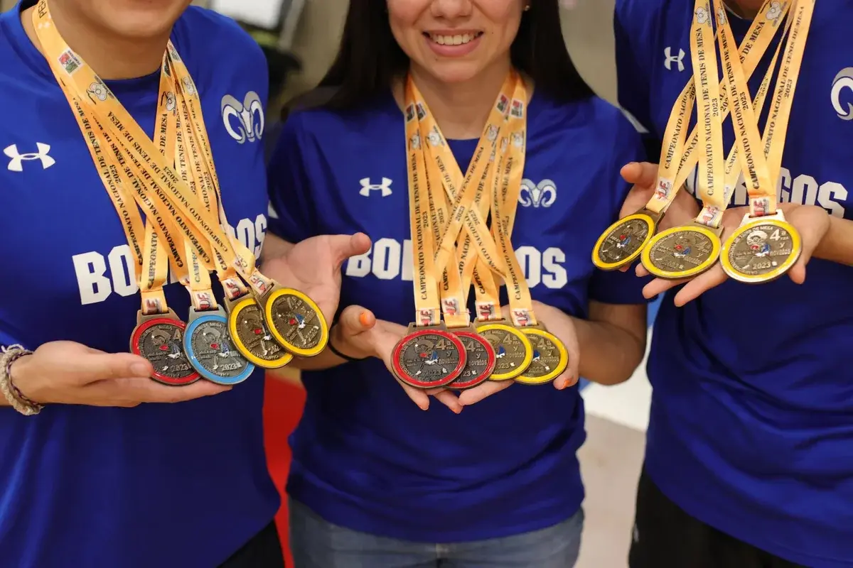 Three young athletes in blue jerseys holding up several medals.