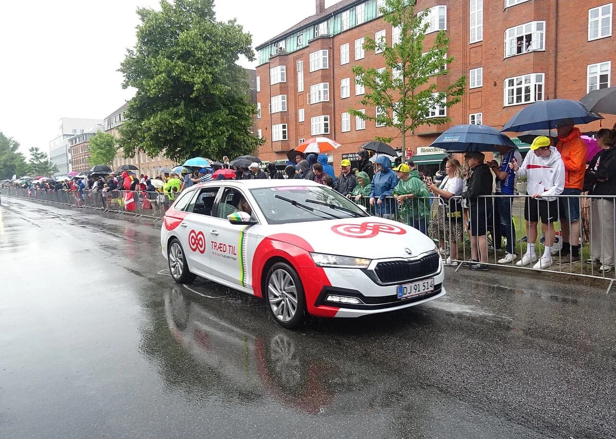 A Kræftens Bekæmpelse promotional car drives past spectators on a rainy street.