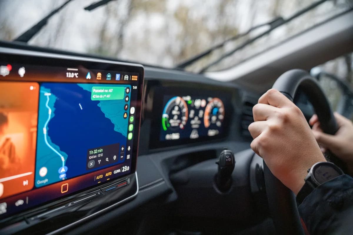 Driver holding a steering wheel with GPS navigation visible on the dashboard display.
