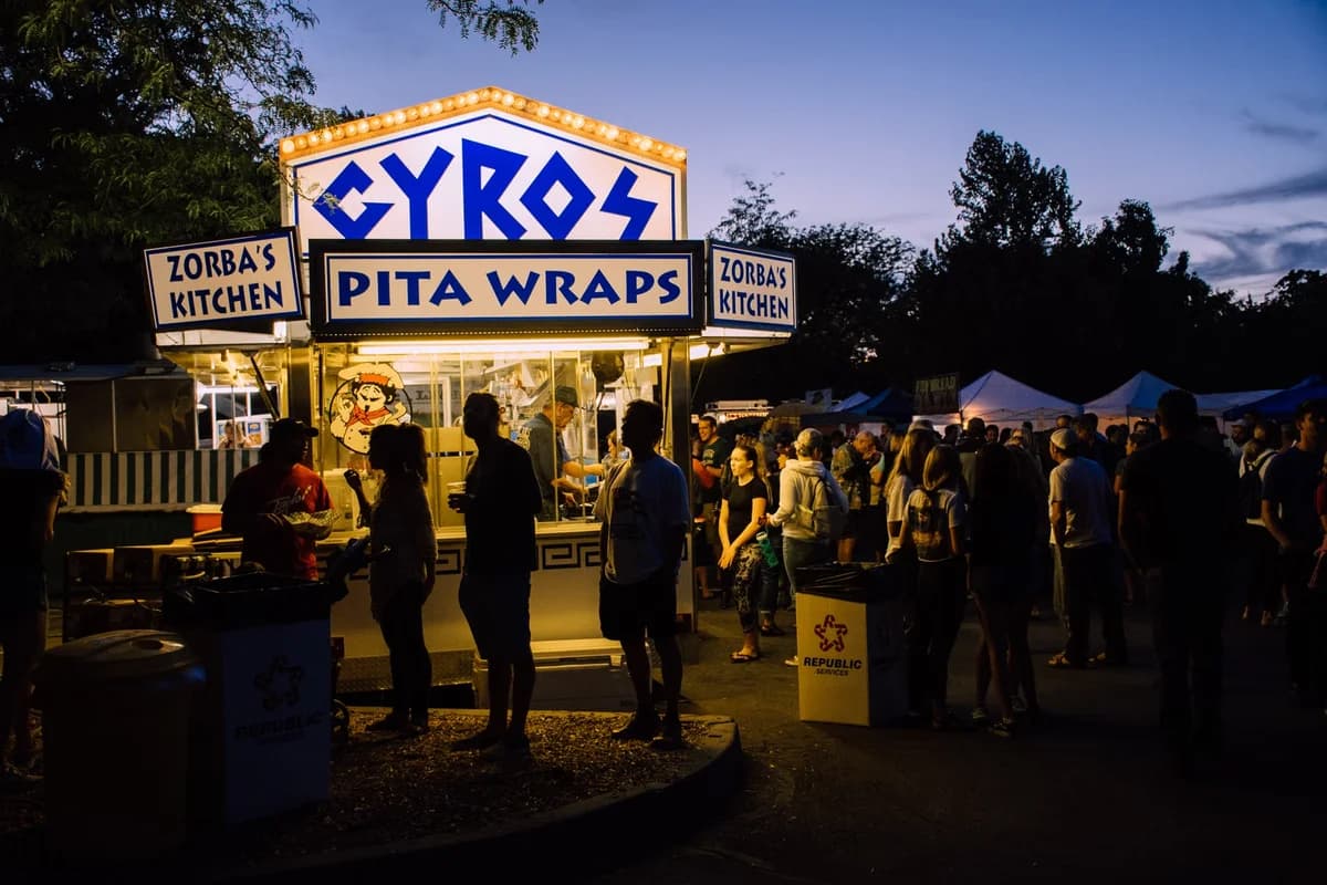 People standing by gyros and pita wraps food stall at evening food festival
