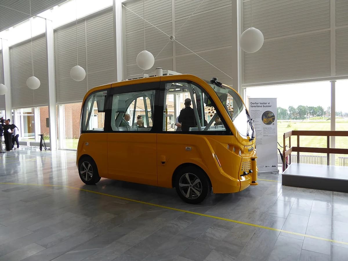 A yellow self-driving bus indoors at a hospital lobby with people nearby.
